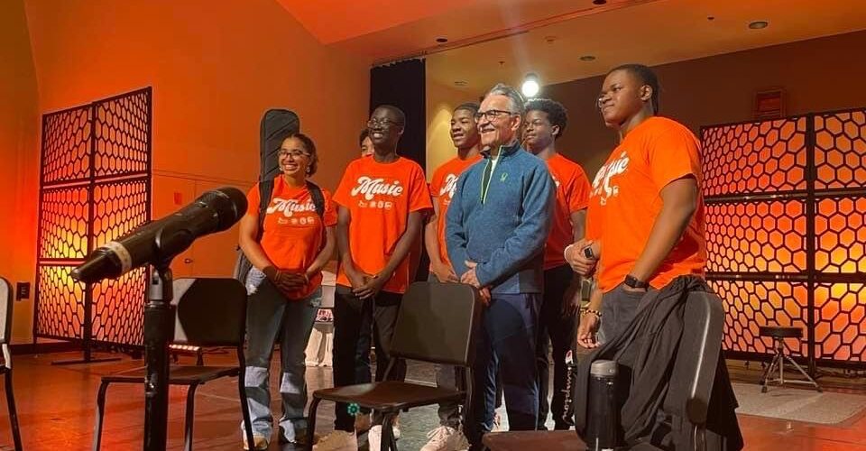 Teenagers with orange Music shirts with older man on a stage