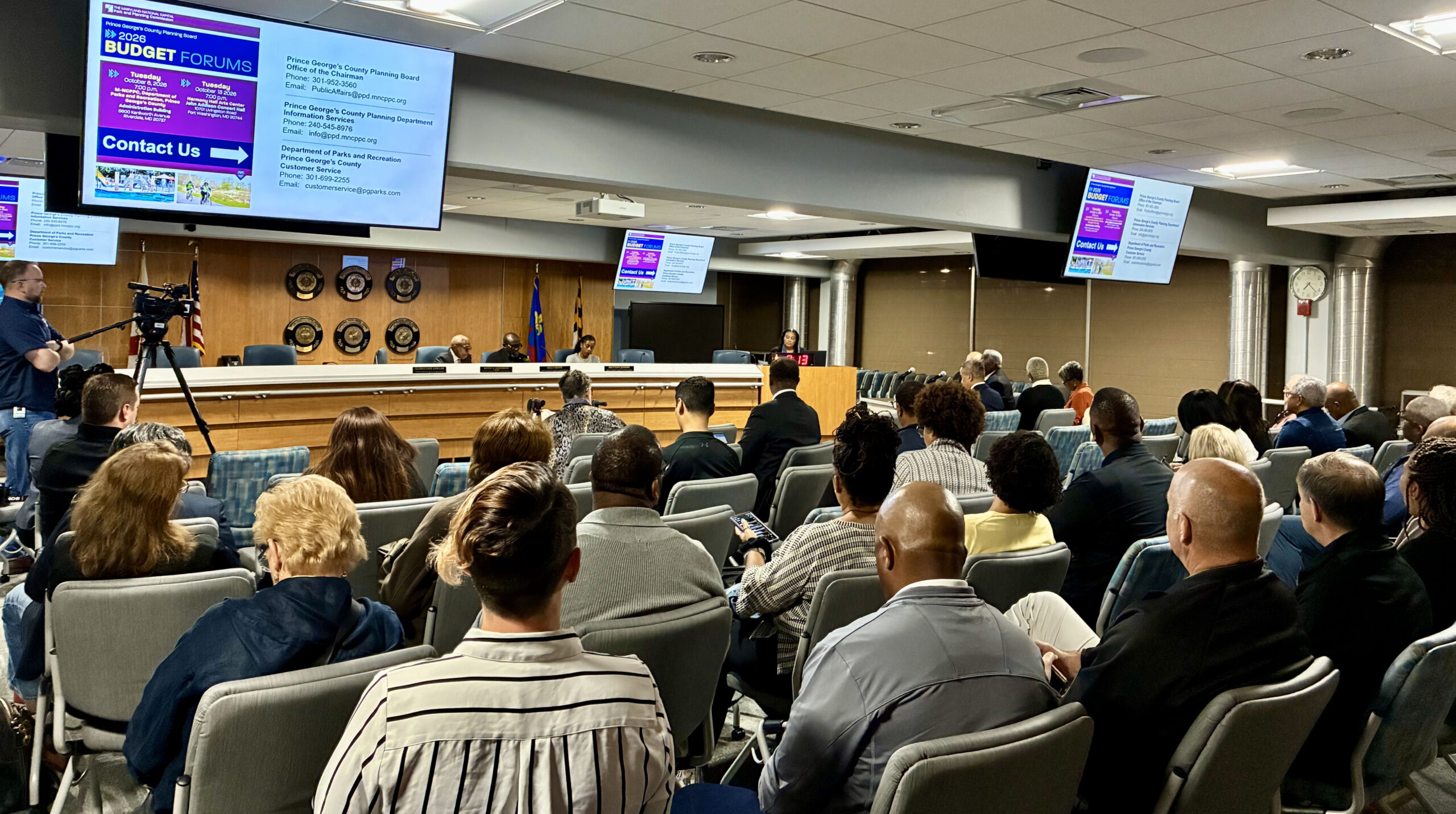 Audience members attend the Prince George’s County Planning Board 2026 Budget Forum in a public meeting room, with presenters seated at the budget forum information displayed on overhead screens.